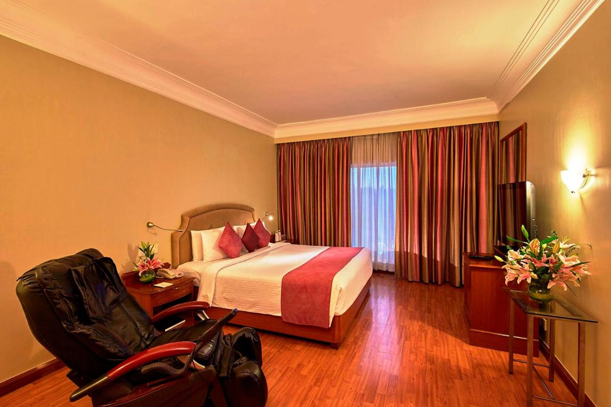 a hotel room with a bed and a chair at Hotel Royal Orchid Bangalore in Bengaluru