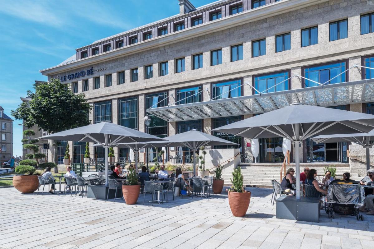 des gens assis à des tables sous des parasols devant un bâtiment dans l'établissement Golden Tulip Saint Malo– Le Grand Bé, à Saint-Malo