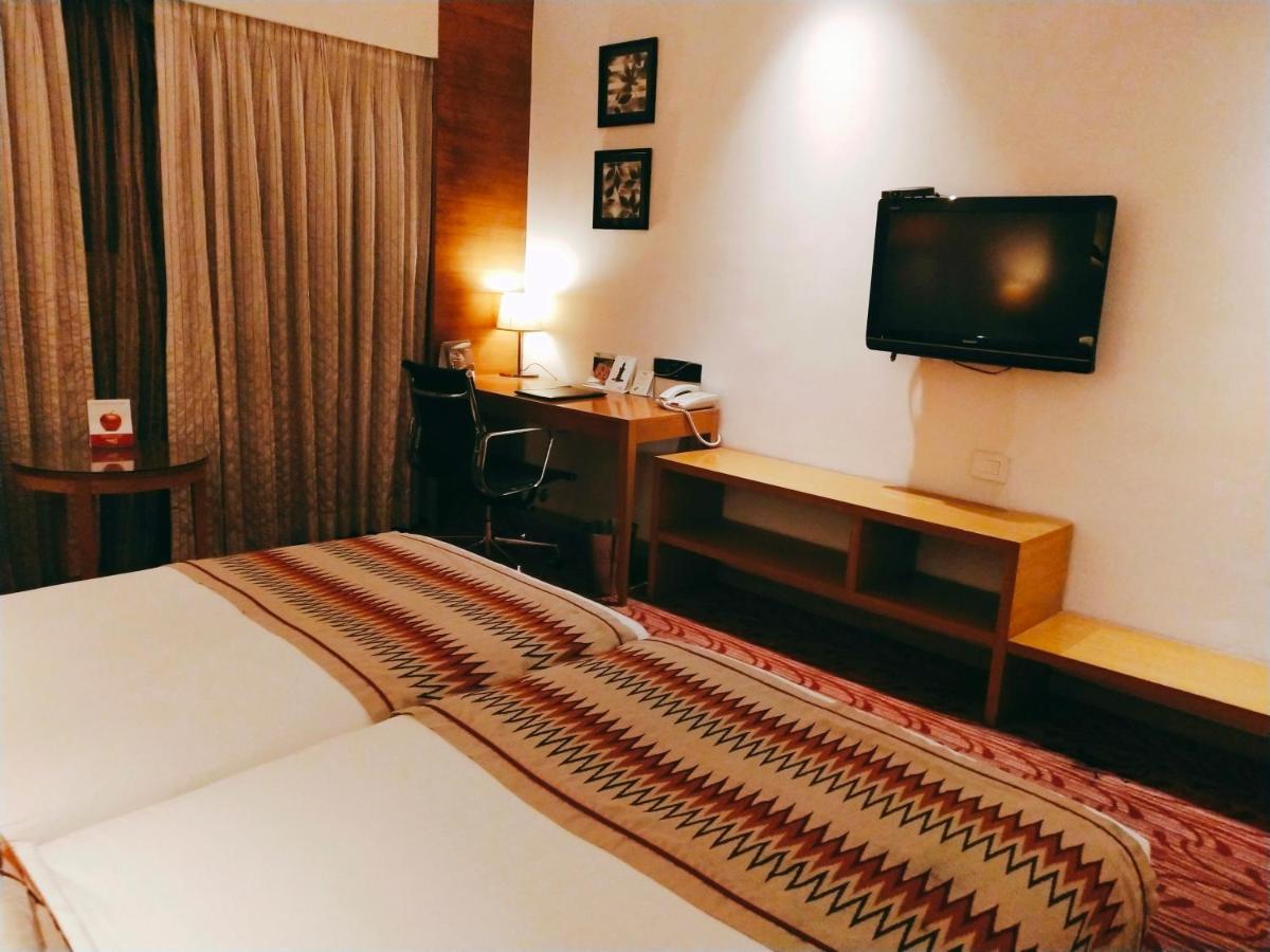 a hotel room with a bed and a desk and a television at Pride Plaza Hotel, Kolkata in Kolkata