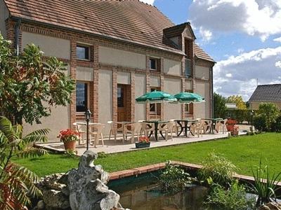 une maison avec un patio avec des tables et des parasols dans l'établissement Logis Hotel Le Nuage, à La Bussière