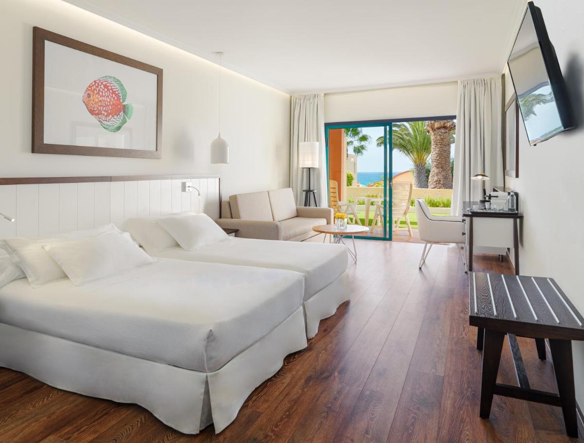 Una habitación de hotel con dos camas y una sala de estar. en H10 Playa Esmeralda - Adults Only, en Costa Calma