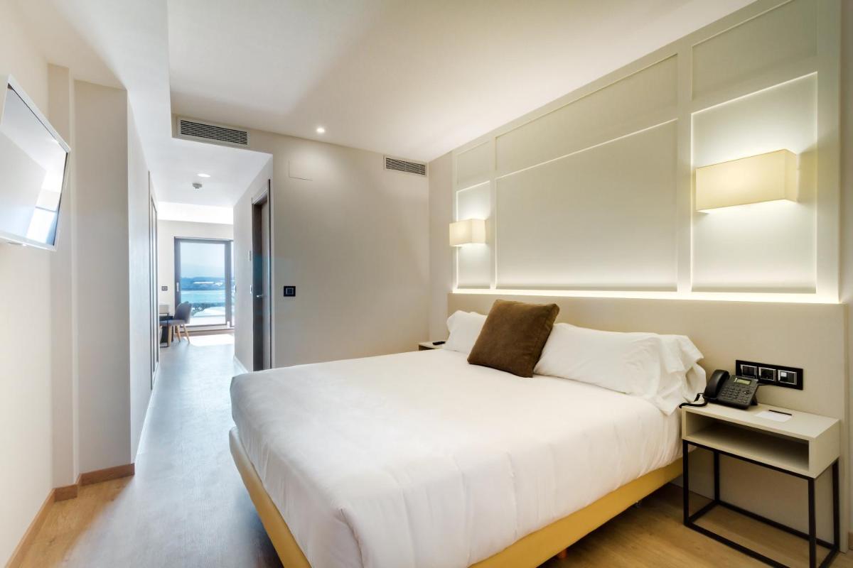 Un dormitorio con una cama blanca y un teléfono en una mesa. en Oca Playa de Foz Hotel & Spa, en Foz