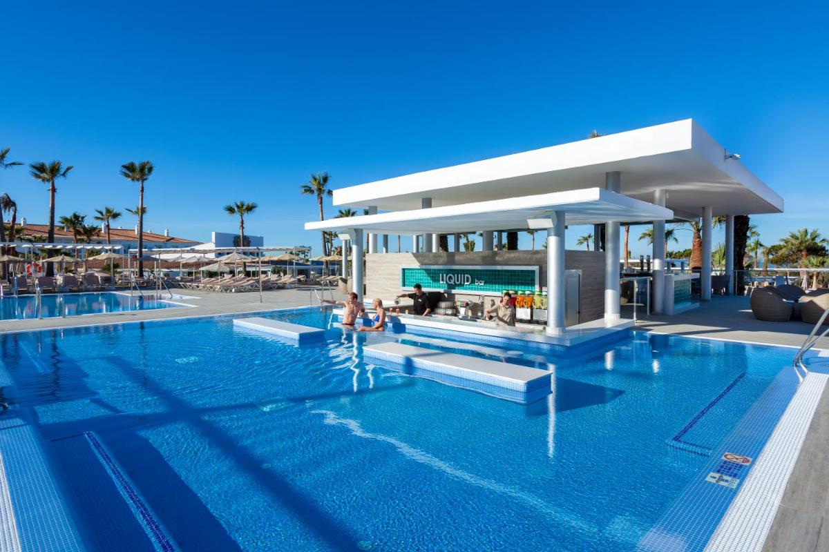 Una piscina en un resort con gente sentada en el agua. en Hotel Riu Chiclana - All Inclusive, en Chiclana de la Frontera