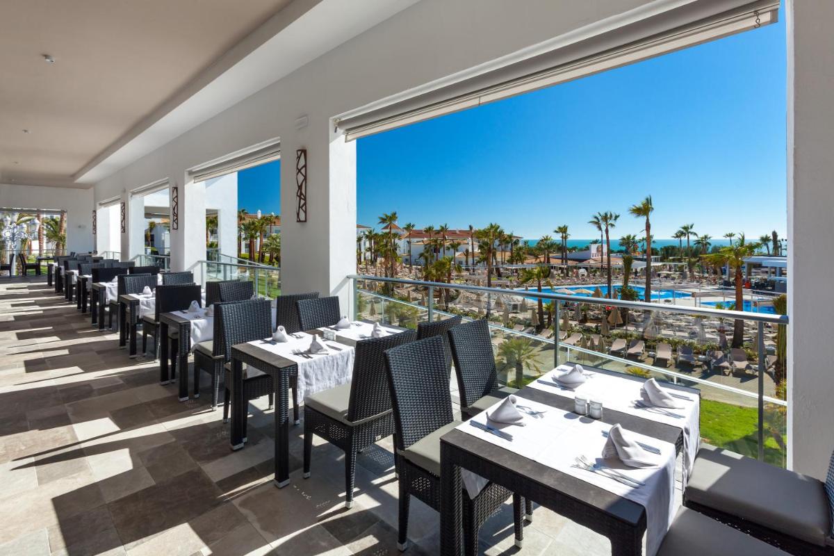 Un restaurante con mesas y sillas y vista al mar. en Hotel Riu Chiclana - All Inclusive, en Chiclana de la Frontera