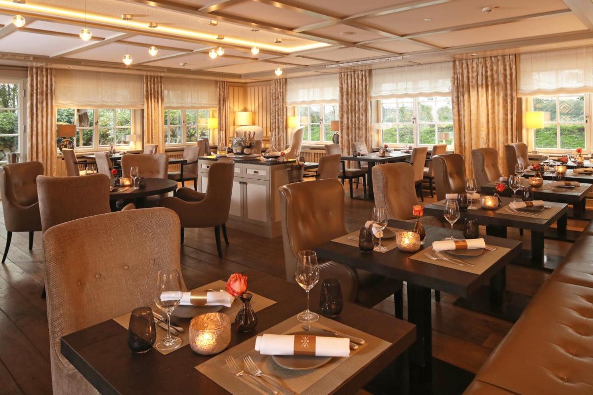 ein Restaurant mit Holztischen und -stühlen und Fenstern in der Unterkunft Severin's Resort & Spa in Keitum