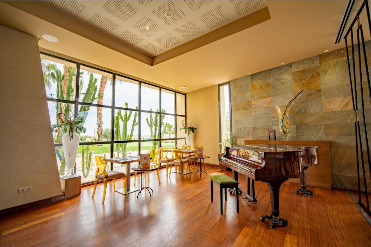 Una habitación con un piano, mesas y ventanas. en Hotel Valle del Este, en Vera