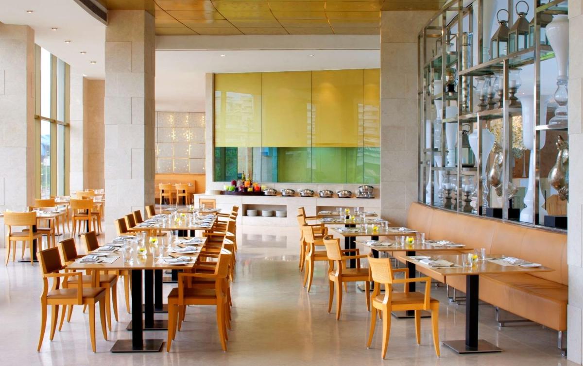 a restaurant with tables and chairs and a kitchen at Radisson Blu Hotel New Delhi Dwarka in New Delhi a restaurant with tables and chairs and a kitchen at Radisson Blu Hotel New Delhi Dwarka in New Delhi