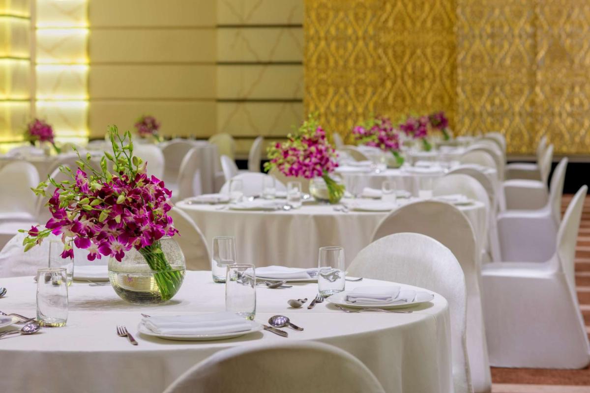 a room filled with tables with white chairs and purple flowers at Radisson Blu Atria Bengaluru in Bengaluru a room filled with tables with white chairs and purple flowers at Radisson Blu Atria Bengaluru in Bengaluru