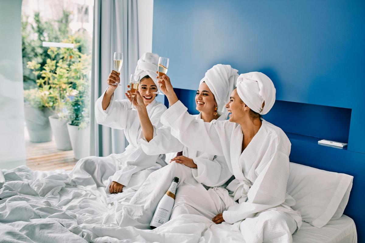 Tres mujeres con batas blancas sentadas en una cama en Ebano Hotel Apartments & Spa, en Playa d'en Bossa