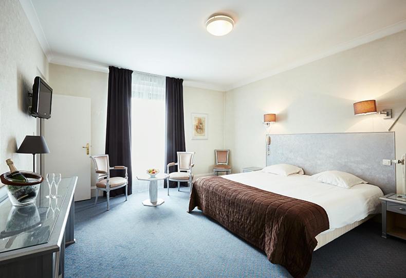 une chambre d'hôtel avec un lit, une table et des chaises dans l'établissement Hôtel Cosmos & Spa, à Contrexéville