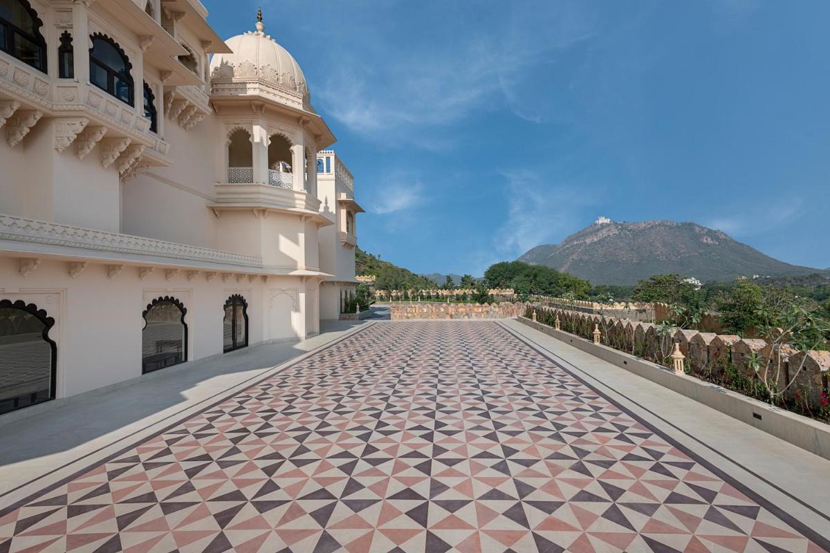 a building with a tiled walkway with a mountain in the background at Aurika, Udaipur - Luxury by Lemon Tree Hotels in Udaipur