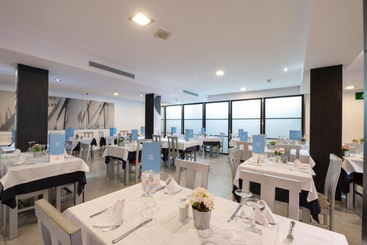 Un restaurante con mesas y sillas blancas y ventanas. en Nautic Hotel & Spa, en Can Pastilla