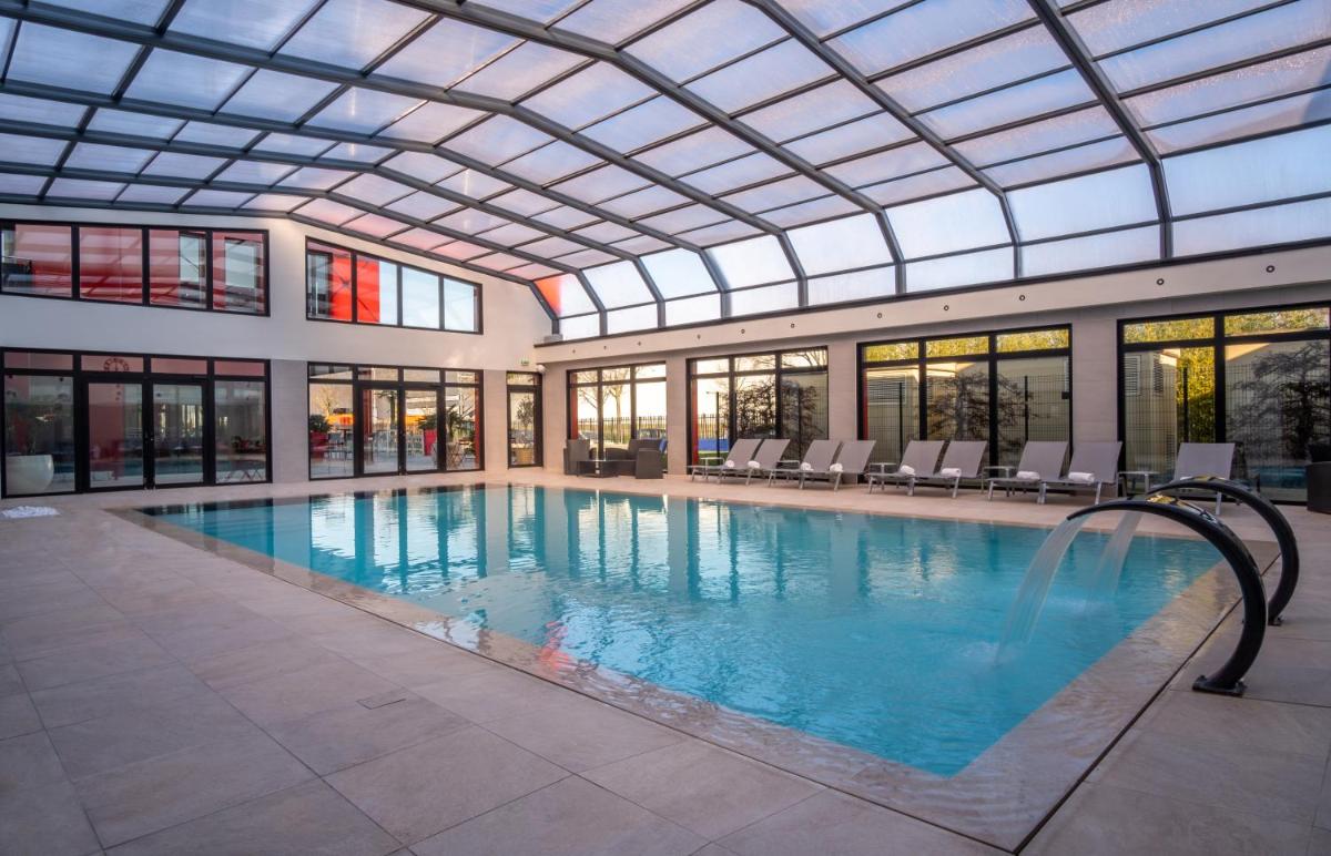 une grande piscine avec un plafond de verre dans l'établissement Kyriad Prestige Lyon Est - Saint Priest Eurexpo Hotel and SPA, à Saint-Priest