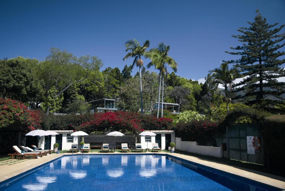 uma piscina com cadeiras, guarda-sóis e árvores em Quinta da Casa Branca - Small Luxury Hotels of the World no Funchal