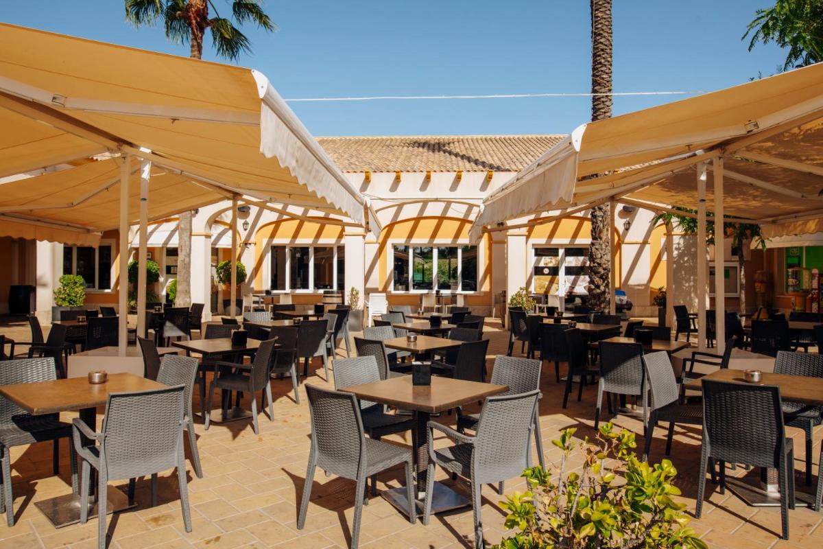 Un restaurante al aire libre con mesas, sillas y sombrillas. en Alannia Costa Blanca, en Crevillente