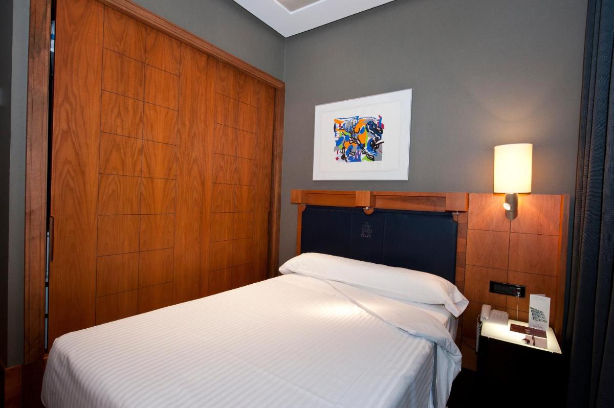 Un dormitorio con una cama blanca y un cabecero de madera. en Gran Hotel Lakua, en Vitoria-Gasteiz