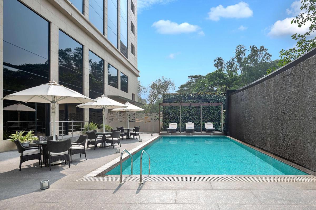 a swimming pool with chairs and umbrellas next to a building at Radisson Mumbai Andheri MIDC in Mumbai a swimming pool with chairs and umbrellas next to a building at Radisson Mumbai Andheri MIDC in Mumbai
