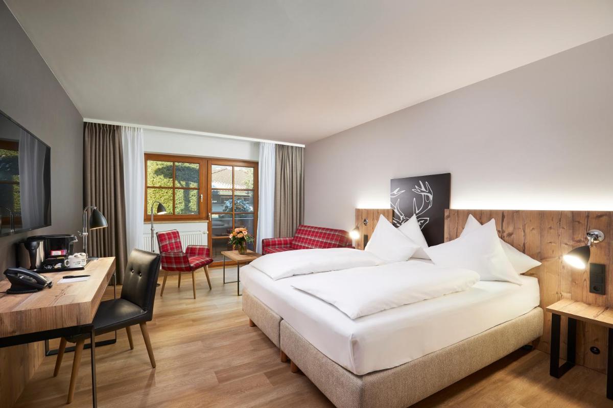 ein Hotelzimmer mit einem Bett, einem Schreibtisch und Stühlen in der Unterkunft HYPERION Hotel Garmisch - Partenkirchen in Garmisch-Partenkirchen