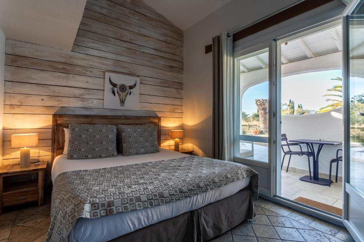 une chambre avec un lit et un balcon avec une table dans l'établissement Le Mas de Cocagne, à Saintes-Maries-de-la-Mer