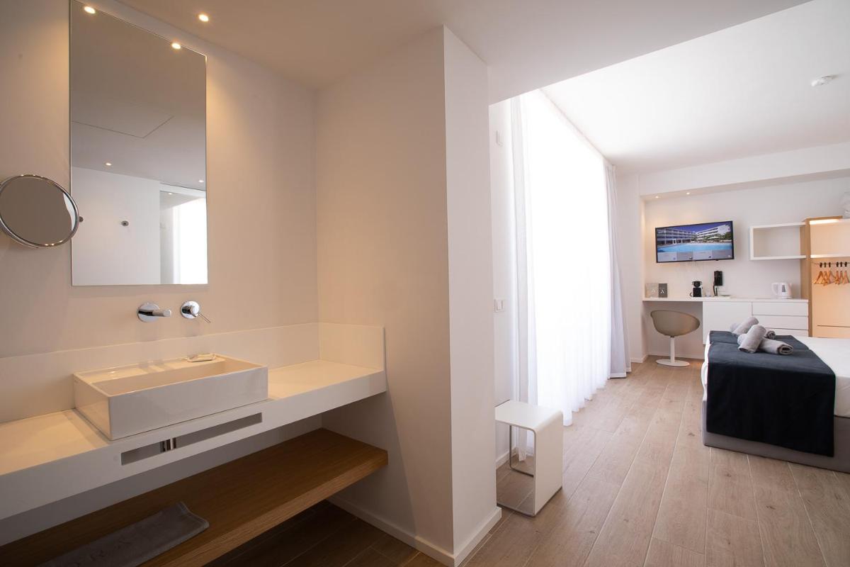 Un baño con lavabo, espejo y cama. en Hotel Anfora Ibiza, en Es Canar