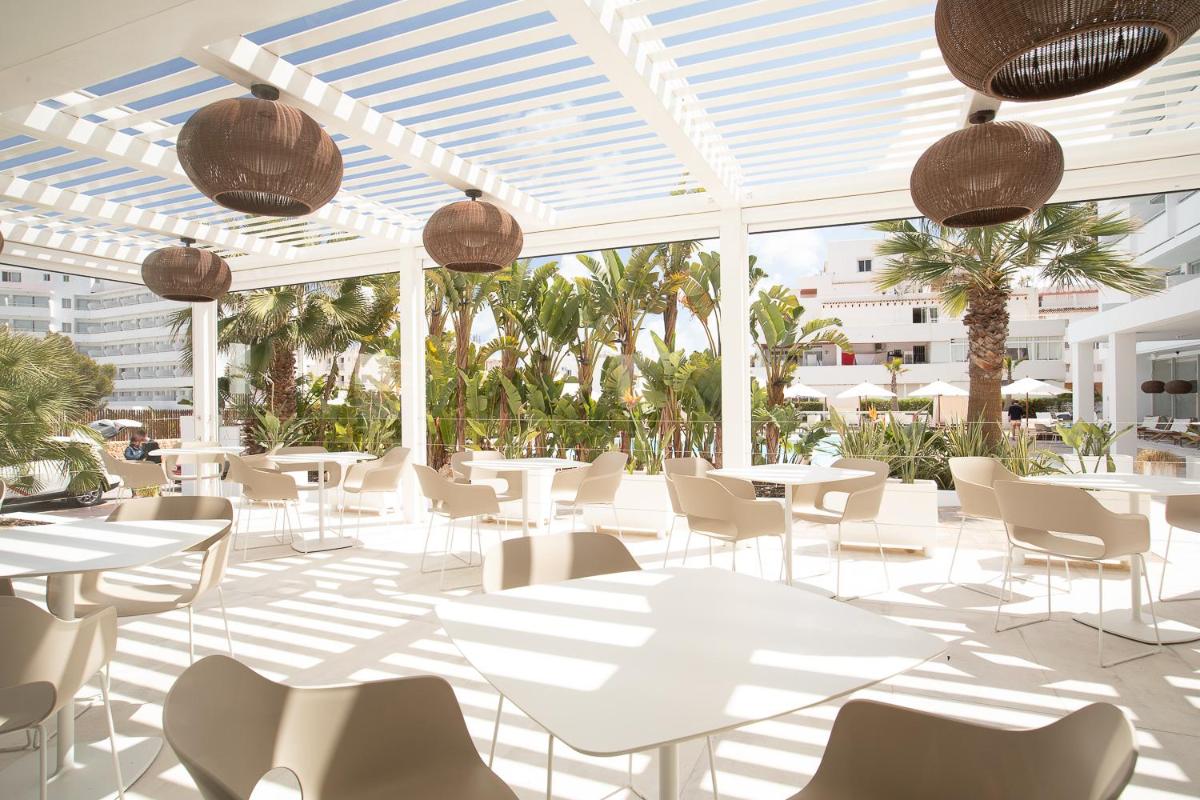 Un restaurante con mesas y sillas blancas y palmeras. en Hotel Anfora Ibiza, en Es Canar