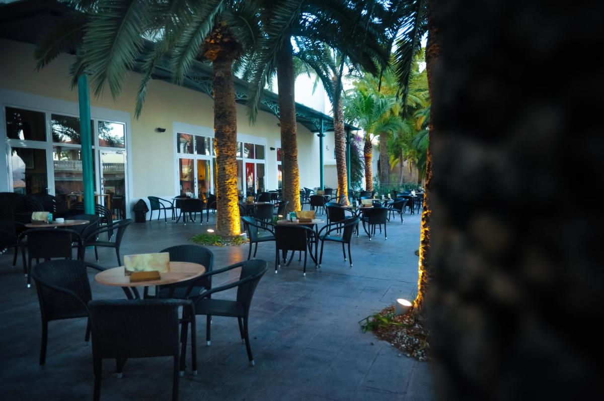 Un patio con mesas y sillas y palmeras. en Balneario de Leana, en Fortuna