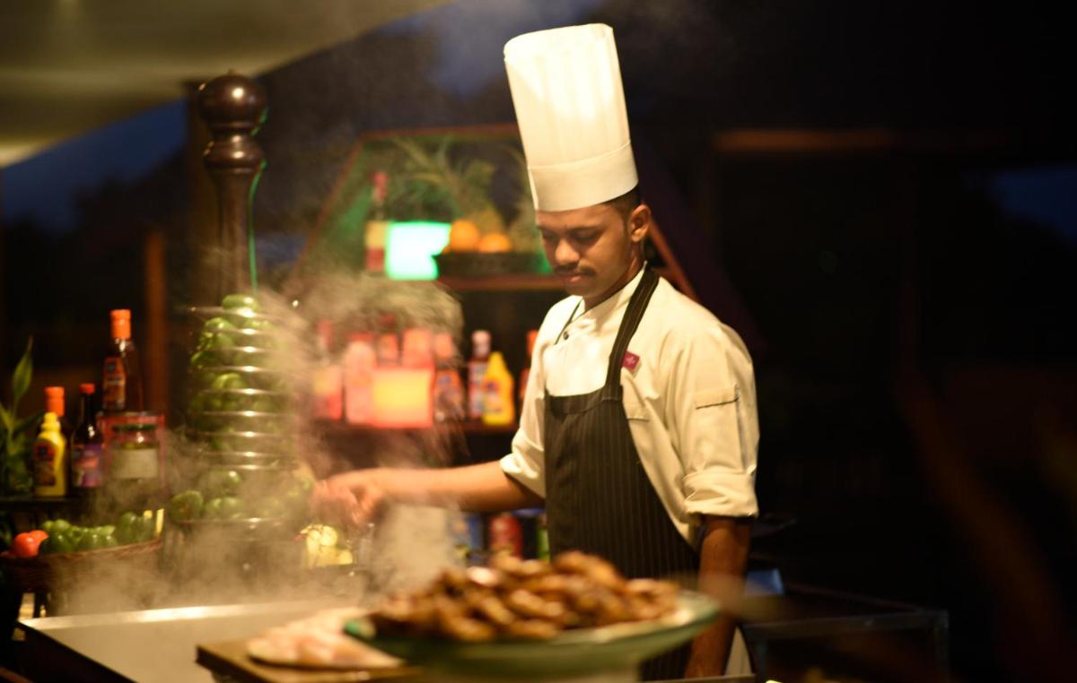 a chef preparing food in a kitchen with a plate of food at Crowne Plaza Kochi by IHG in Cochin