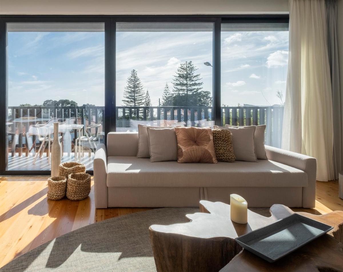 uma sala de estar com um sofá e uma janela grande em Aqua - Pópulo Eco Village em Ponta Delgada