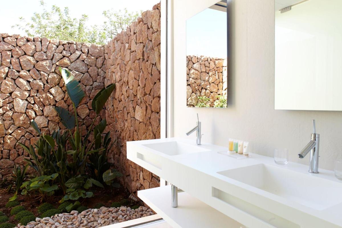 baño con 2 lavabos y pared de piedra en Ca Na Xica - Hotel & Spa, en Sant Miquel de Balansat