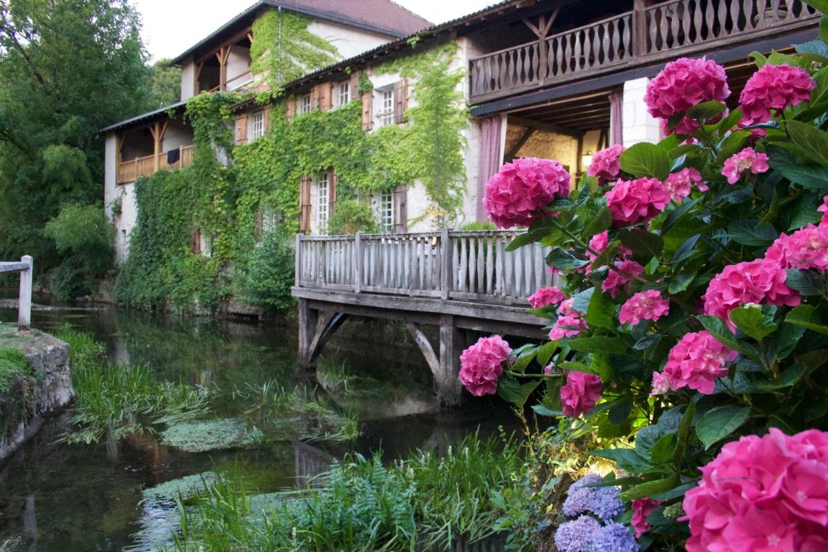 un pont sur un ruisseau devant une maison fleurie dans l'établissement Le Moulin du Roc, à Brantôme