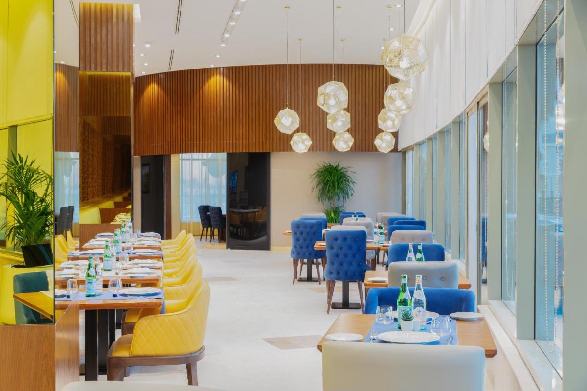 a dining room with tables and blue chairs at Barcelo Al Jaddaf, Dubai in Dubai a dining room with tables and blue chairs at Barcelo Al Jaddaf, Dubai in Dubai