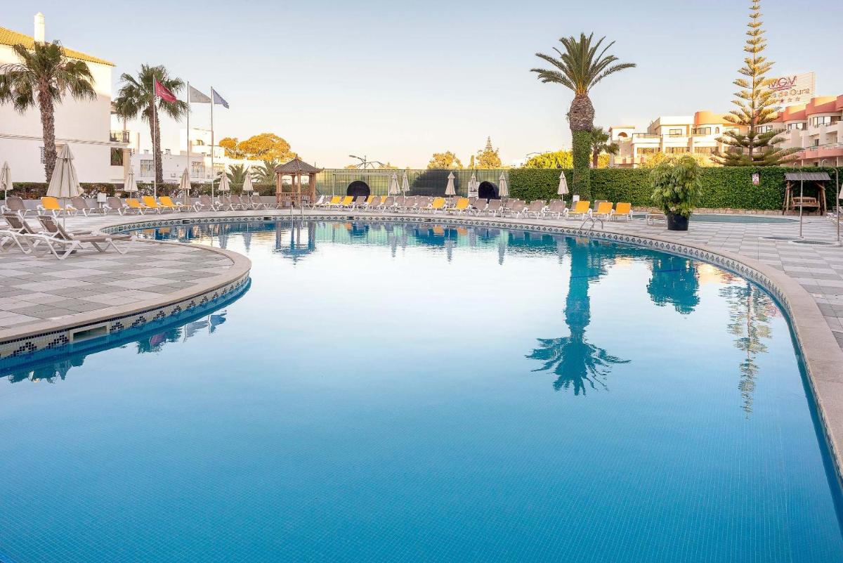 uma grande piscina azul com cadeiras e palmeiras em Muthu Oura Praia Hotel em Albufeira