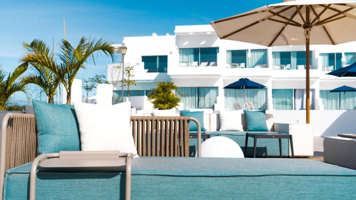 un patio con sillas y sombrilla y un edificio en CalaLanzarote Suites Hotel - Adults Only 16years, en Playa Blanca