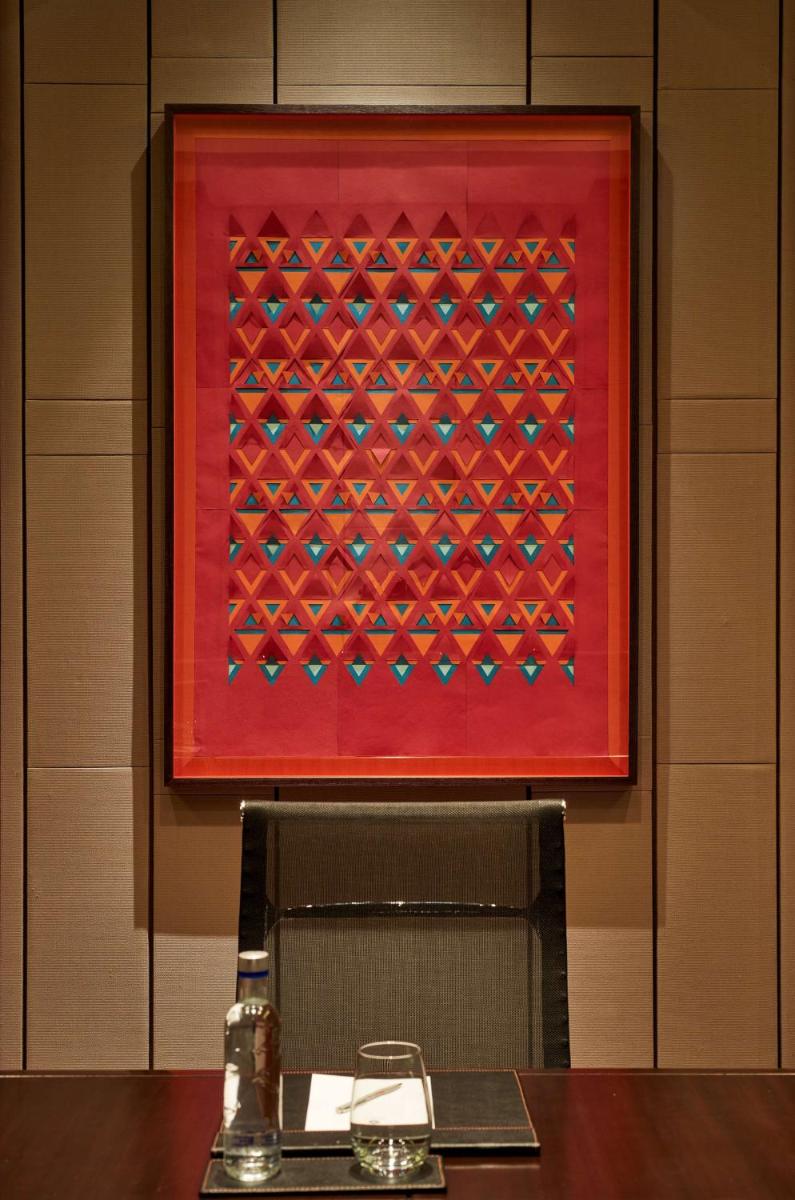 a red painting on the wall above a table with a glass at Hyatt Regency Chandigarh in Chandīgarh