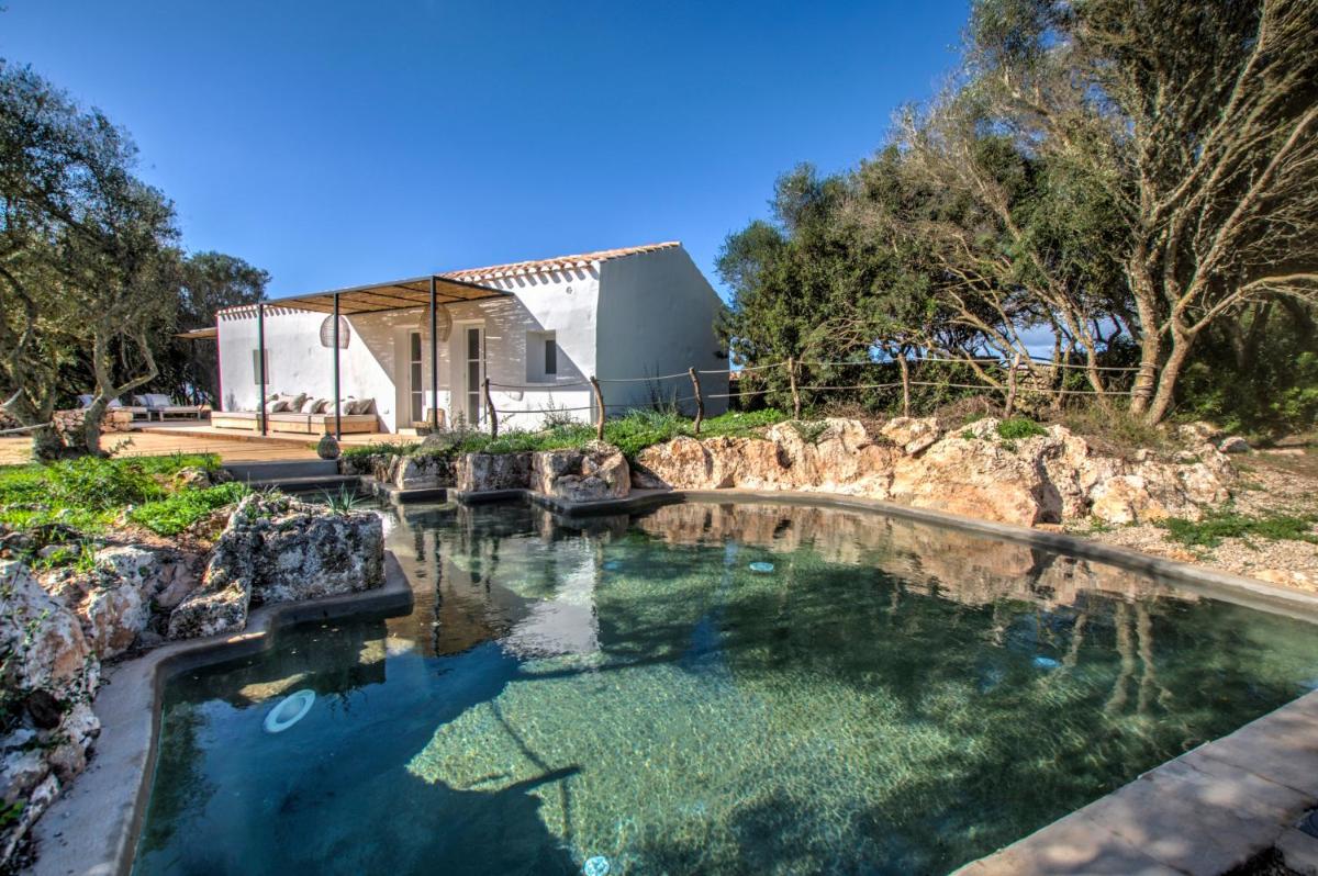 una piscina de agua con una casa en el fondo en Torre Vella Fontenille Menorca, en Son Bou