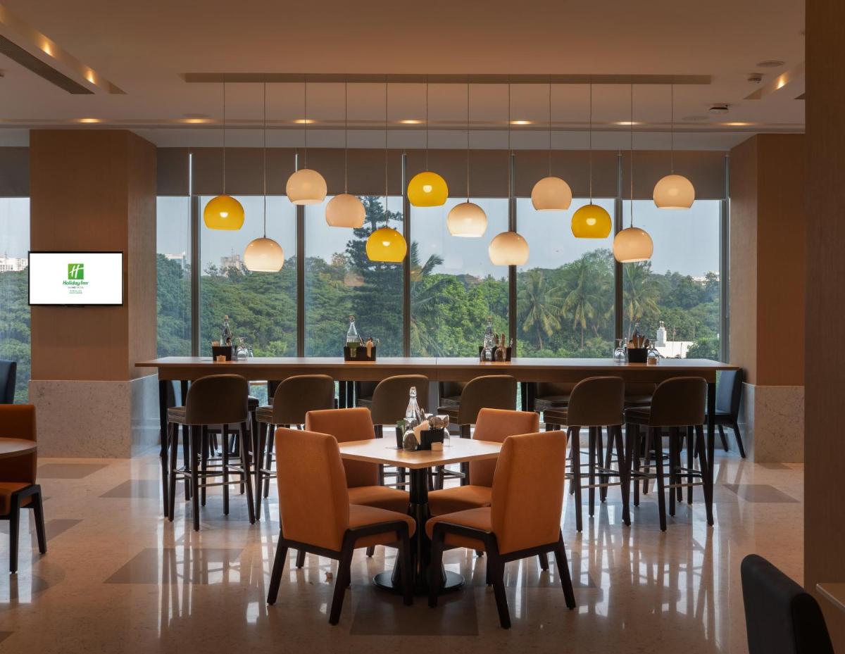 a restaurant with tables and chairs and large windows at Holiday Inn Bengaluru Racecourse by IHG in Bengaluru a restaurant with tables and chairs and large windows at Holiday Inn Bengaluru Racecourse by IHG in Bengaluru