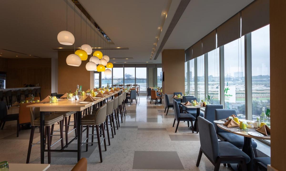 a restaurant with tables and chairs and large windows at Holiday Inn Bengaluru Racecourse by IHG in Bengaluru a restaurant with tables and chairs and large windows at Holiday Inn Bengaluru Racecourse by IHG in Bengaluru