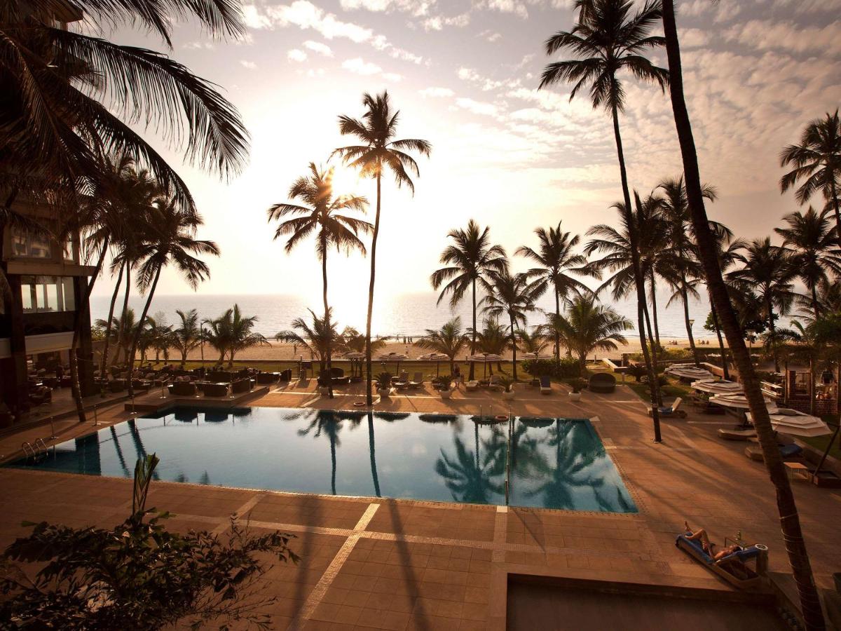 a view of a pool with palm trees and the ocean at Novotel Mumbai Juhu Beach in Mumbai