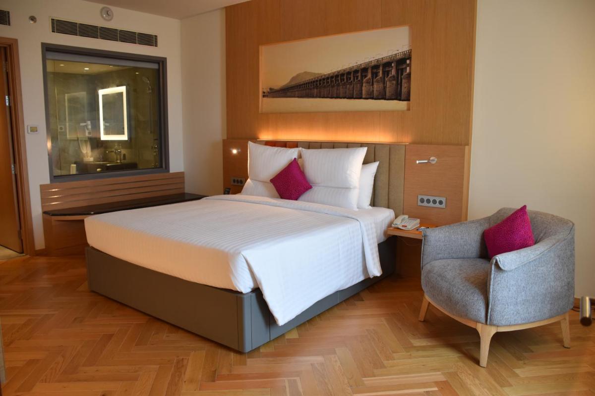 a hotel room with a bed and a chair at Novotel Vijayawada Varun in Vijayawāda