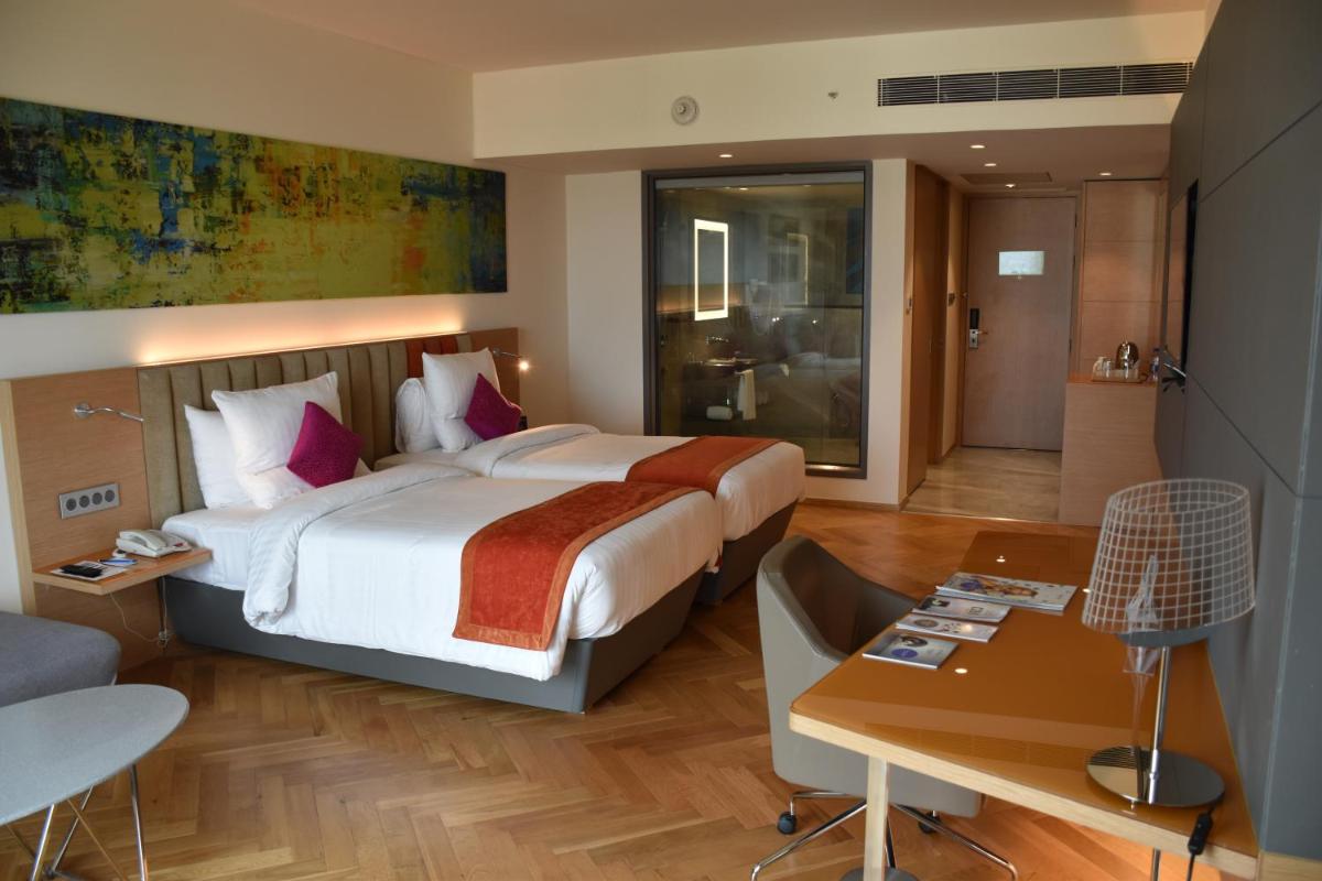a hotel room with a large bed and a desk at Novotel Vijayawada Varun in Vijayawāda