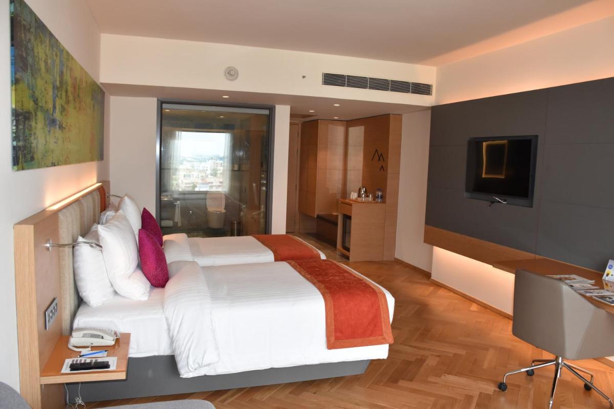 a bedroom with a white bed and a television at Novotel Vijayawada Varun in Vijayawāda
