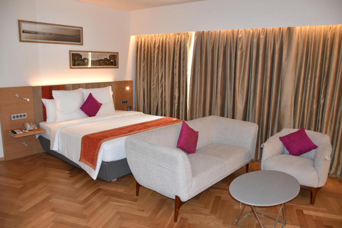 a hotel room with a bed and two chairs at Novotel Vijayawada Varun in Vijayawāda