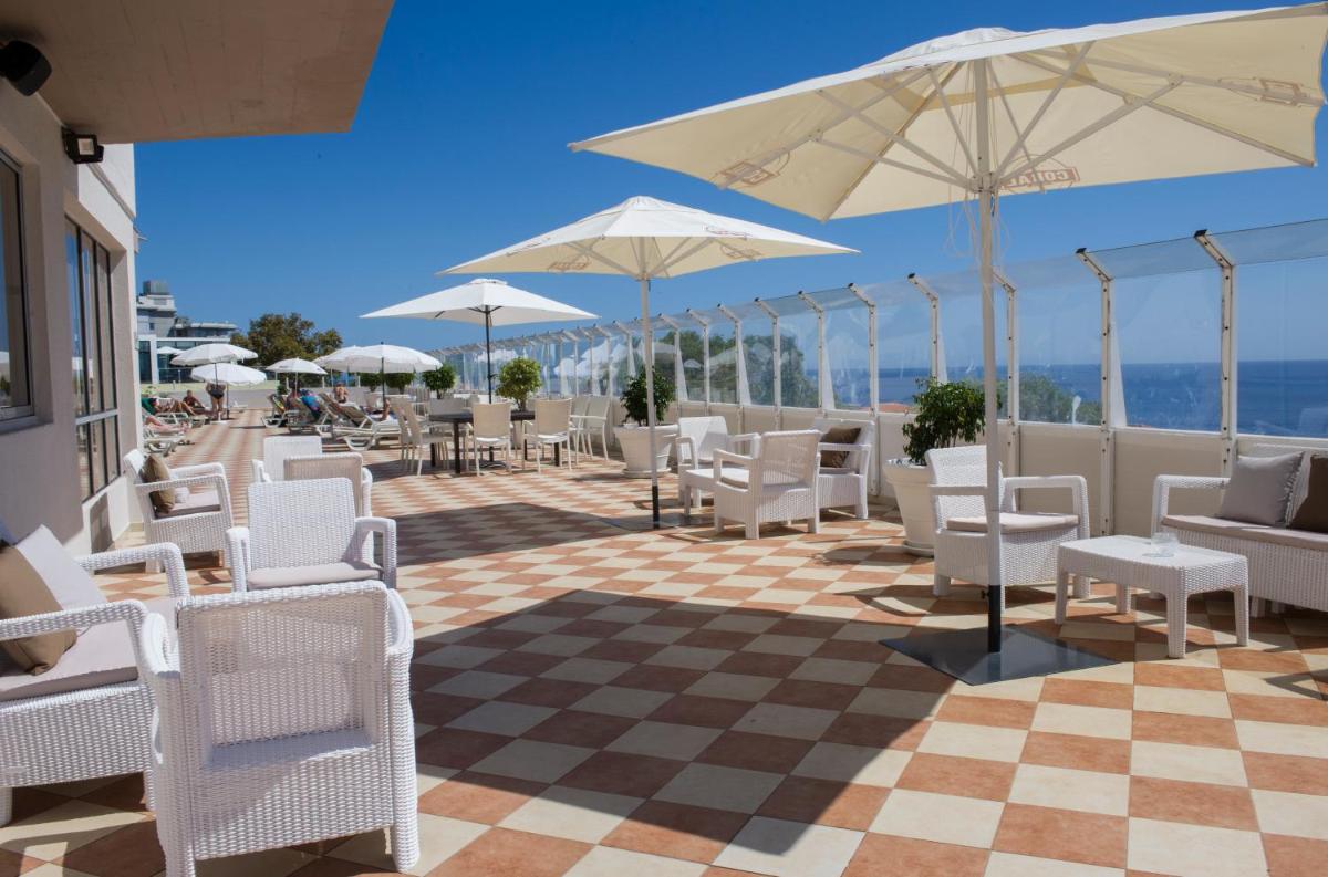 um pátio com cadeiras brancas, mesas e guarda-sóis em Florasol Residence Hotel - Dorisol hotels no Funchal