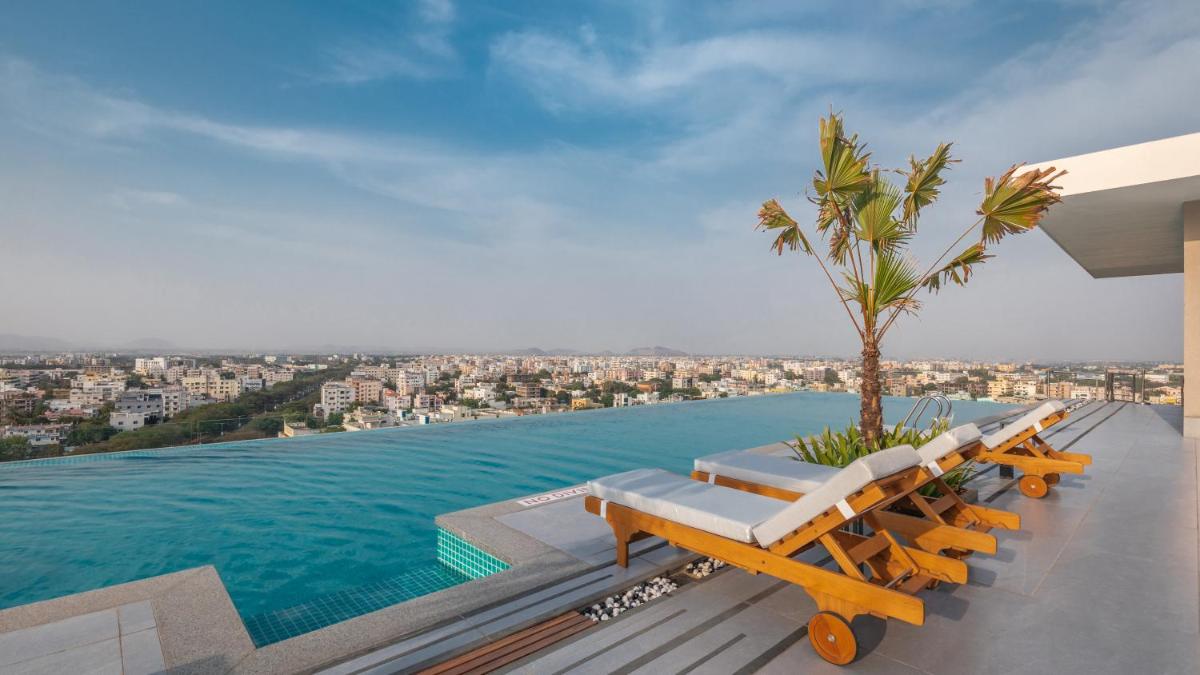 a pool with lounge chairs and a palm tree on a house at Novotel Vijayawada Varun in Vijayawāda