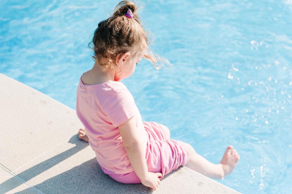 una niña sentada en el borde de una piscina en Hotel Mas Solà, en Santa Coloma de Farners