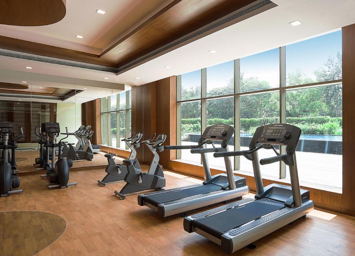 a gym with several tread machines in a room with windows at Radisson Blu Plaza Hotel Mysore in Mysore