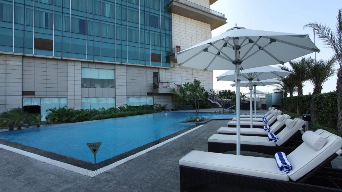 a swimming pool with white lounge chairs and an umbrella at Crowne Plaza New Delhi Rohini by IHG in New Delhi a swimming pool with white lounge chairs and an umbrella at Crowne Plaza New Delhi Rohini by IHG in New Delhi