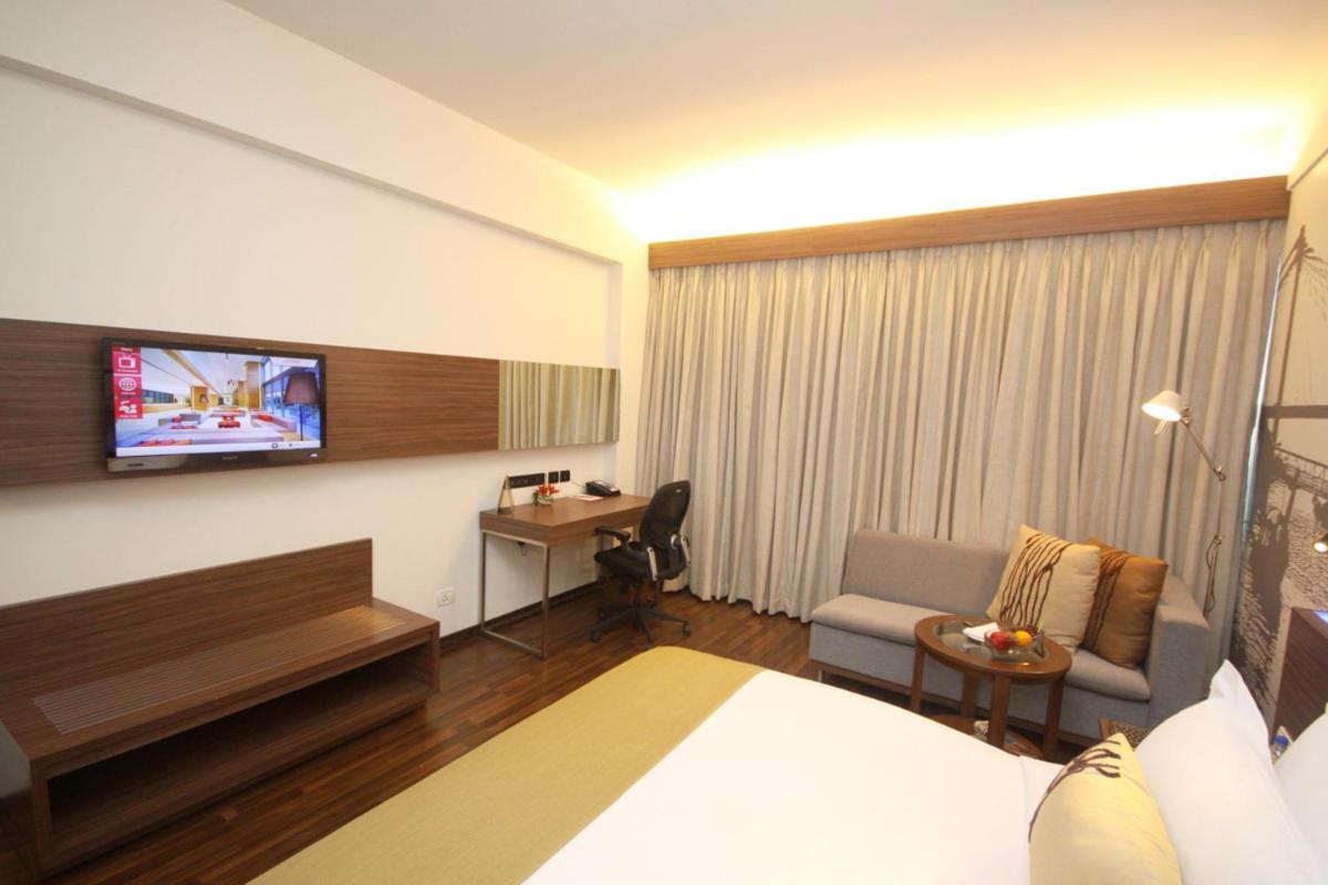 a hotel room with a bed and a desk and a television at Vivanta Kolkata EM Bypass in Kolkata