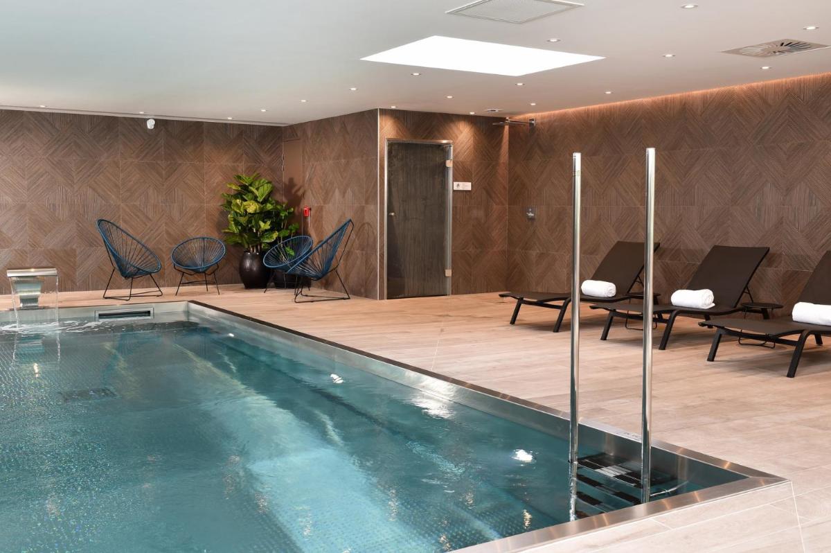 une piscine dans le hall d'un hôtel avec des chaises et des tables dans l'établissement Oceania Saint Malo, à Saint-Malo