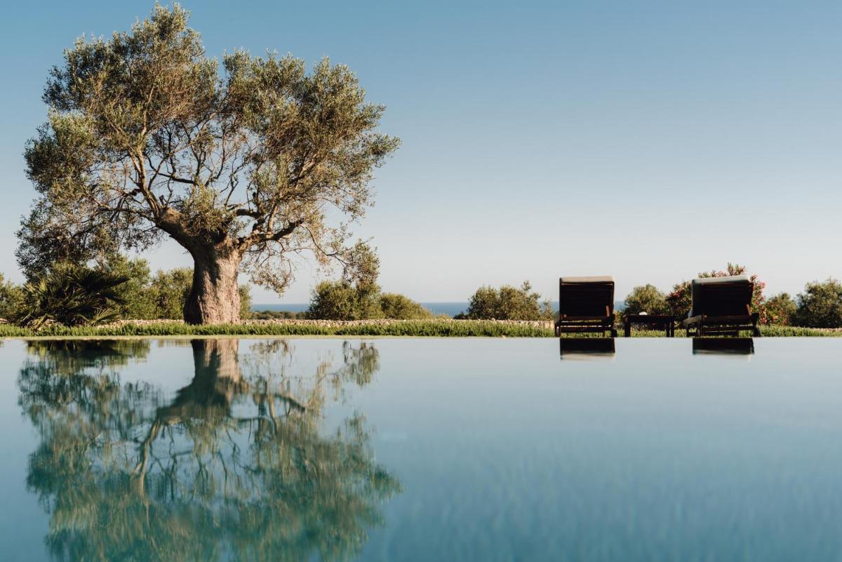 Dos sillas y un árbol al lado de un cuerpo de agua. en Torralbenc, a Small Luxury Hotel of the World, en Cala'n Porter